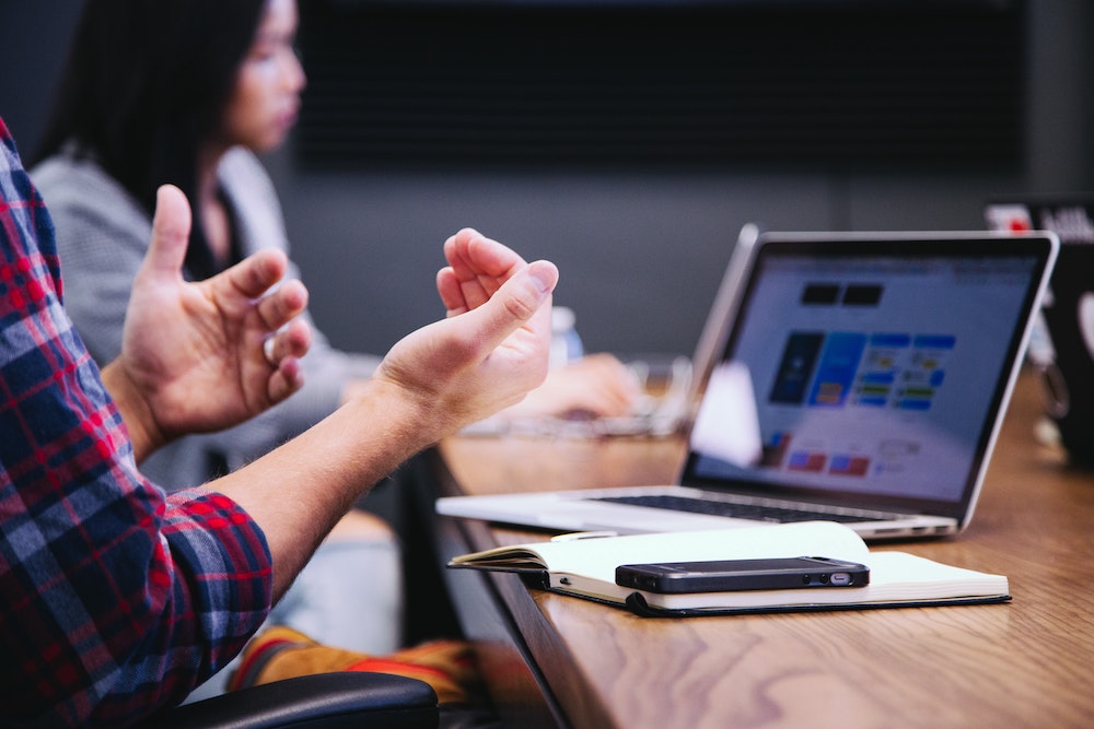 A man's hand gestures in front of a laptop screen